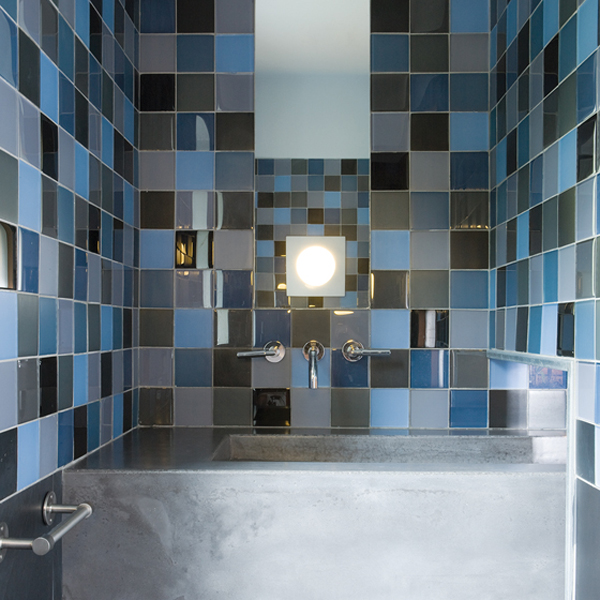 A powder room in Maryland is a symphony of blue-glass tiles with a custom concrete sink. INTERIOR DESIGN: ColePrévost PHOTOGRAPHY: Angie Seckinger