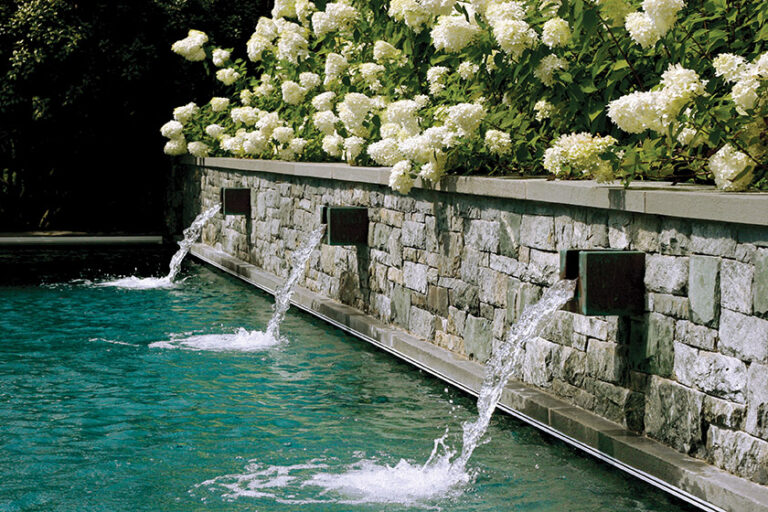 A pool in Washington, DC, features a stone wall and three custom scuppers, softened by an elegant hydrangea backdrop. LANDSCAPE ARCHITECTURE: Colao & Peter Outdoor Environments PHOTOGRAPHY: François Verhoeven