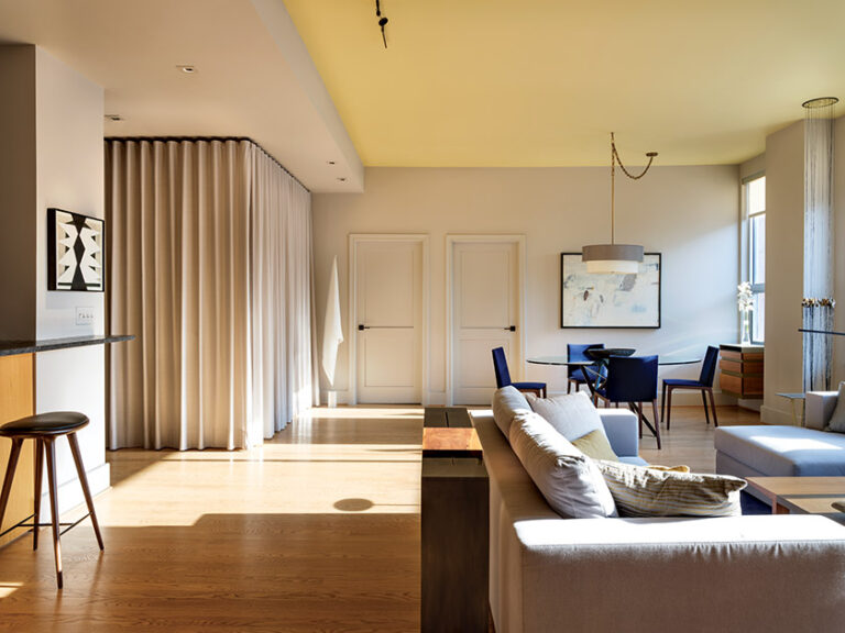 A curtain hides an unsightly plethora of doors for utility services, creating a serene backdrop for the dining room; the console behind the sofa was designed by ColePrévost. INTERIOR DESIGN: ColePrévost PHOTOGRAPHY: ANGIE SECKINGER