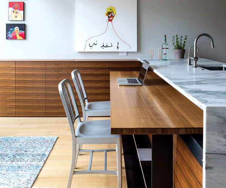 In a renovated DC duplex, a custom, solid-white oak table that slides into the kitchen island can be used as a work surface or pulled out for dining; white oak, black walnut and hot-rolled steel provide a muted backdrop for the white marble counter top and art. INTERIOR DESIGN: ColePrévost PHOTOGRAPHY: Angie Seckinger