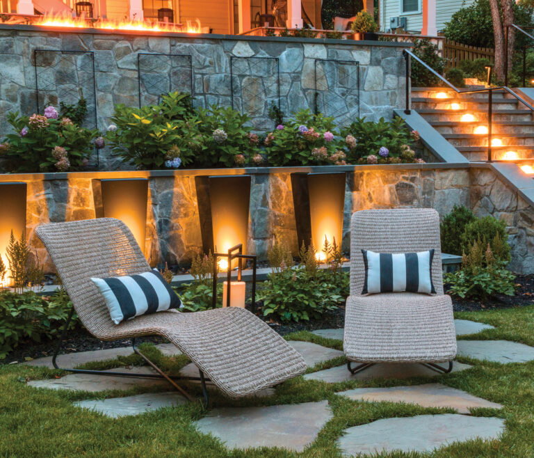 Stone retaining walls and subtle uplighting are a backdrop for an intimate gathering spot atop irregular stone pavers; well-lit steps connect multiple seating areas.