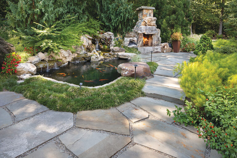 A tiered flagstone patio connects a rustic fireplace made of natural boulders to a garden pond with a waterfall. LANDSCAPE ARCHITECTURE: Surrounds Landscape Architecture + Construction PHOTOGRAPHY: Morgan Howarth