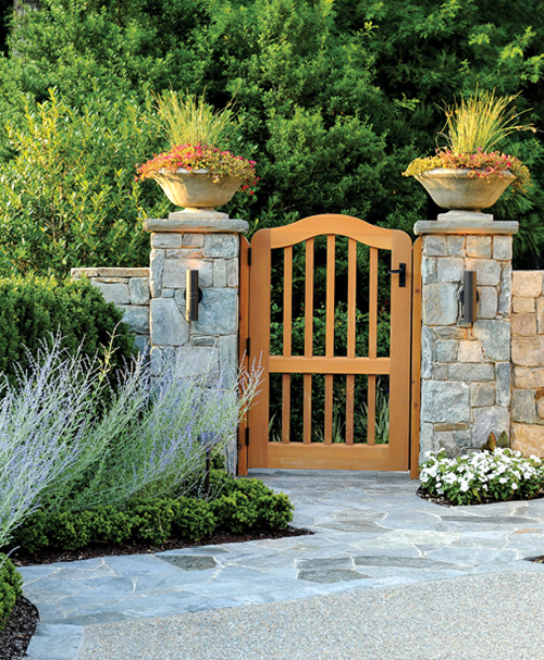 A garden entry feature incorporates a custom cedar gate anchored by large stone columns accented by decorative pots with seasonal annual displays. LANDSCAPE ARCHITECTURE: Surrounds Landscape Architecture + Construction PHOTOGRAPHY: Bob Narod
