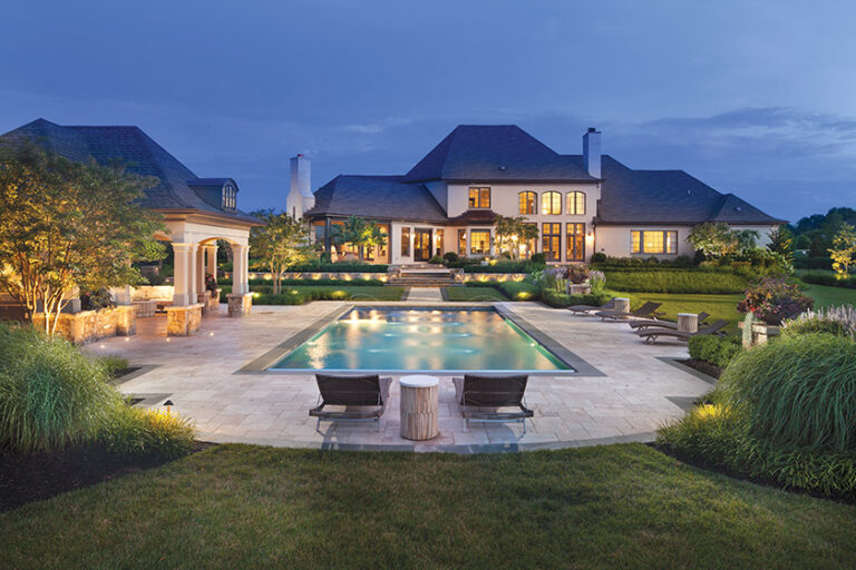 A French Country-inspired pool scape boasts a travertine patio, custom pool house and lush plants. LANDSCAPE ARCHITECTURE: Surrounds Landscape Architecture + Construction PHOTOGRAPHY: Morgan Howarth