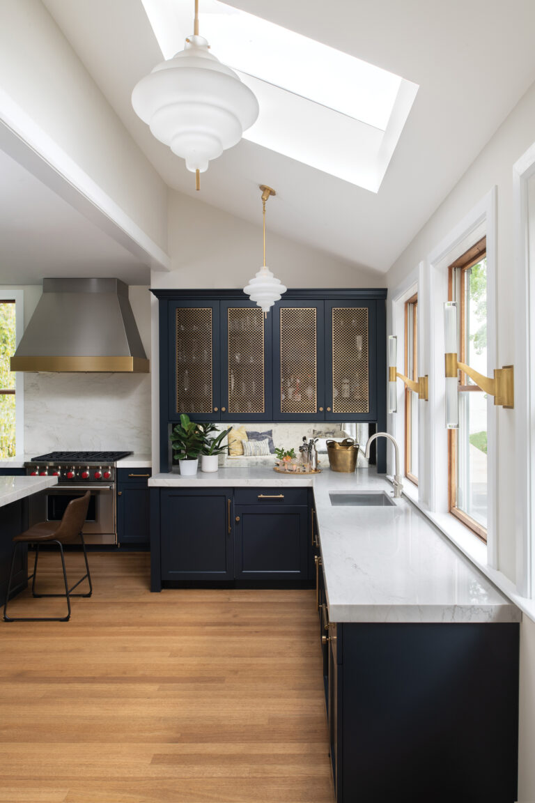 Sculptural lighting and dark-painted cabinets with mesh inserts transform the wet bar area of a kitchen into a moody cocktail lounge.
