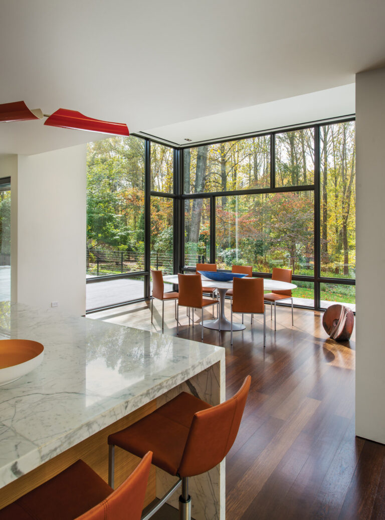 A Torroja cross chandelier by David Weeks is suspended over a kitchen island; anchoring the dining area are Tibet counter stools by KFF, a special edition 96-inch Knoll Tulip table and Nivo armless chairs from KFF. INTERIOR DESIGN: Baron Gurney Interiors, LLC PHOTOGRAPHY: Anice Hoachlander
