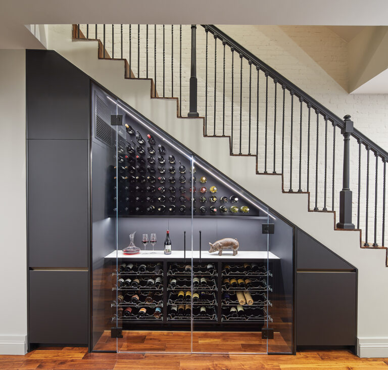 An under-stair wine room introduces unexpected flair to a DC row house kitchen. The refrigerated space features custom glass doors and pullout wire shelves; cabinets to the left and right provide storage. ARCHITECTURE: CARNEMARK / KONST PHOTOGRAPHY: Anice Hochlander