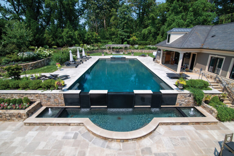 An expansive pool features a weir wall, which forms a waterfall while also creating a separate kiddie pool.