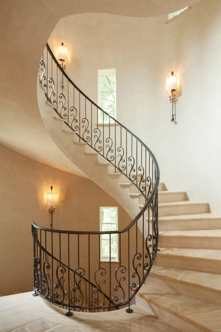 A dramatic limestone staircase with a wrought-iron railing rises in the turret. ARCHITECTURE: Harrison Design PHOTOGRAPHY: Gordon Beall