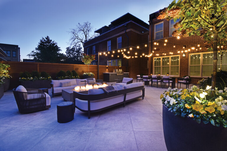 Lit with festoon lights, an Alexandria courtyard features a porcelain-tile patio, ceramic fire table and custom grill cabinet.