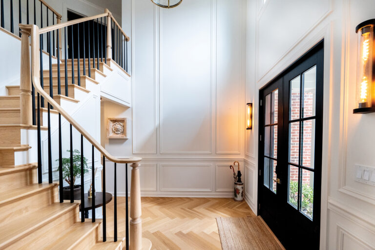 The entry to a Vienna home highlights extensive architectural detailing, herringbone flooring and an oak staircase with contrasting black balusters.