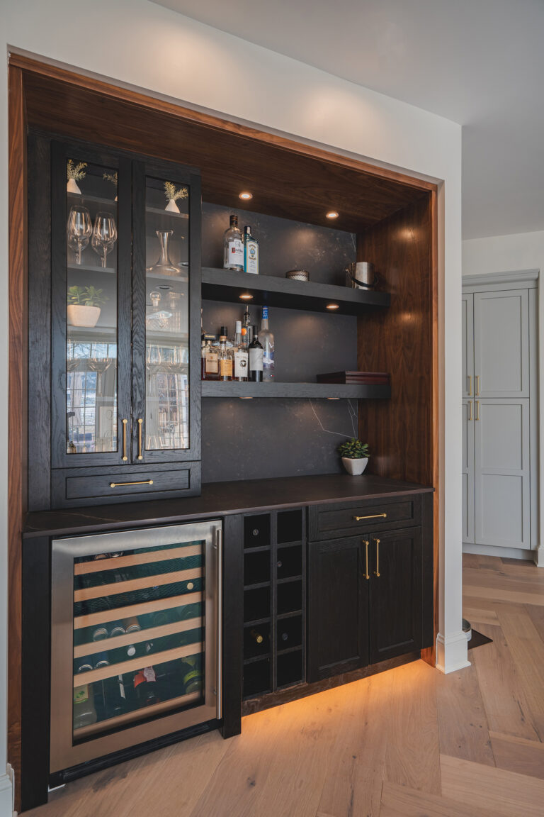 In a Potomac residence, a chic custom bar beckons with integrated lighting, glass-front storage and a built-in wine fridge.