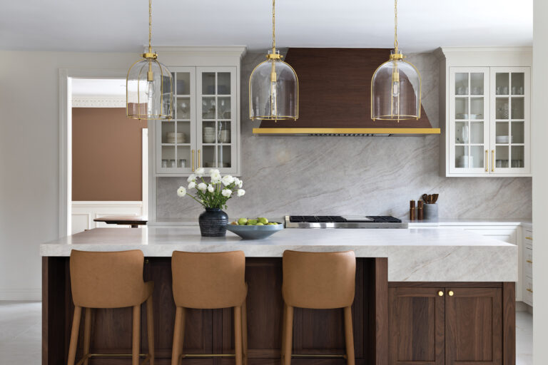 In a Potomac kitchen, walls clad in swirling stone are a backdrop for walnut cabinetry and brass accents on lighting and hardware.