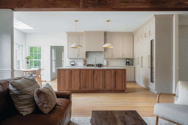 An airy, open-concept kitchen in Vienna features a walnut island, soft-white cabinetry, a marble backsplash and brass pendant lighting.