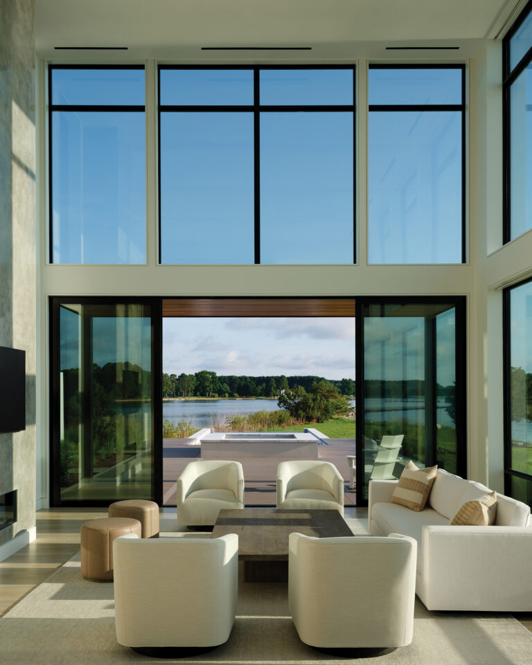 Double-height windows and low-slung, neutral furnishings highlight a light-filled, tech-forward great room boasting indoor-outdoor connectivity.