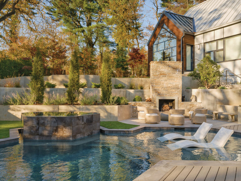 A fieldstone fireplace anchors a poolscape clad in Timbertech composite decking and porcelain pavers.