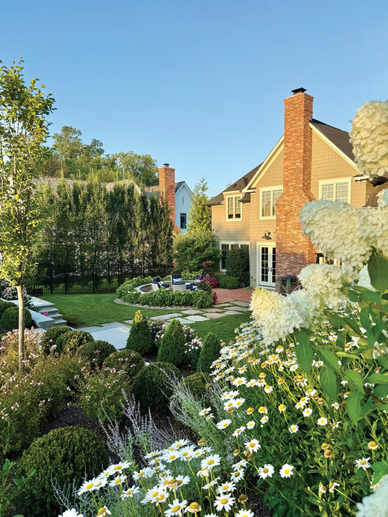 Limelight hydrangea and daisies frame views of a boxwood-fringed garden terrace.